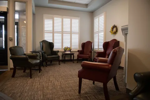 Sitting area with green and burgundy armchairs, shuttered windows and a flower arrangement