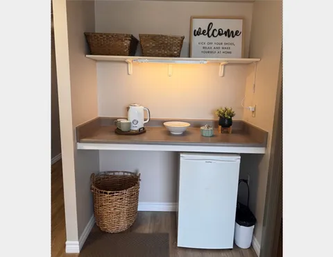 Alcove with a small refrigerator, kettle, countertop and baskets on a shelf
