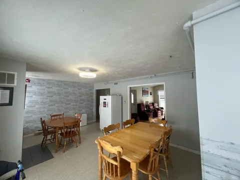 Dining area with wooden tables and chairs, a refrigerator and a doorway into a lounge.