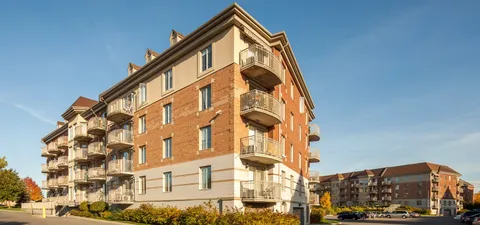 Brick residence building with balconies and landscaped borders beneath a blue sky
