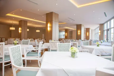 Dining room with white tablecloths, pale chairs and broad windows