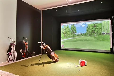 Golf simulator with clubs, a green floor and a screen showing a golf course