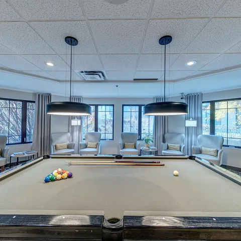 Billiard table with balls and armchairs beside windows