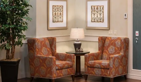Two patterned armchairs beside a small table, lamp and framed prints