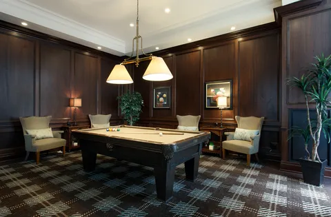Pool table and armchairs in a wood-panelled games room.