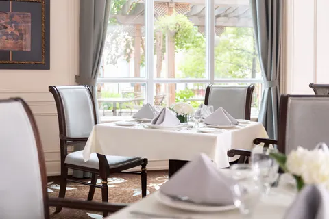 Dining tables beside large windows, set with glassware and flowers.