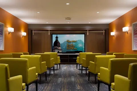 Theatre room with rows of green chairs facing a screen.
