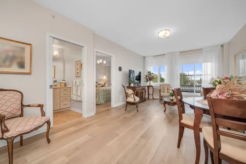 Common room with tables, chairs, wood flooring and large windows.
