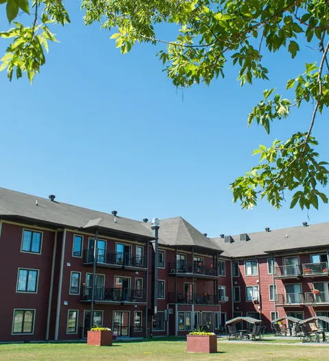 Three-storey building with balconies beside a lawn and trees