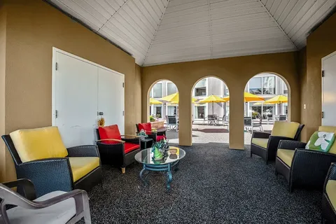 Covered patio with wicker chairs facing a courtyard with yellow umbrellas