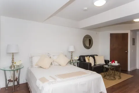Studio bedroom with a white bed, black sofa, round mirror and wooden floor