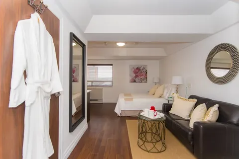 Studio with a bed, black sofa, wall mirrors and a white robe by the doorway