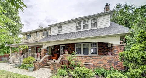 Brick and white-sided house with a covered porch, lawn and flower planters