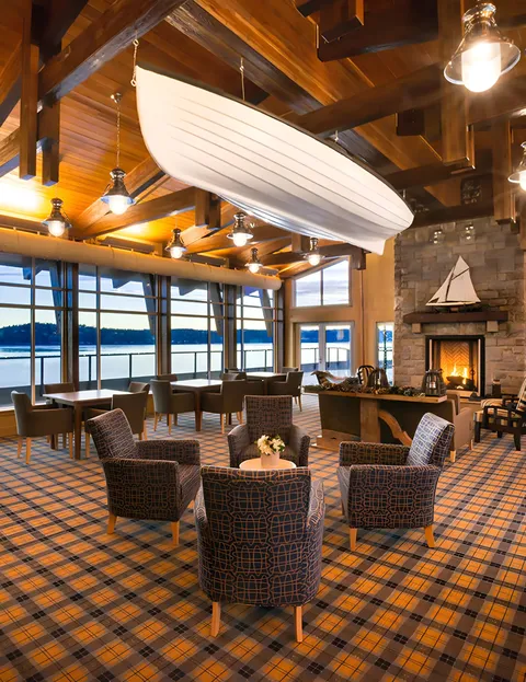 Lounge with a fireplace, upholstered chairs and a boat suspended from the wood ceiling.