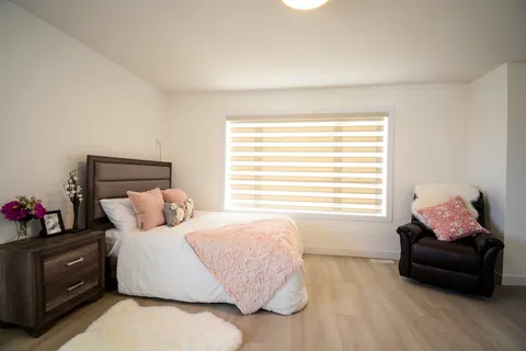 Bedroom with a bed, pink cushions and throw, a bedside table and a reclining armchair