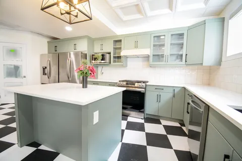 Kitchen with green cabinets, an island, a stainless steel refrigerator and a black-and-white tiled floor
