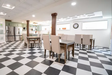 Dining room with tables, upholstered chairs, green kitchen cabinets and a black-and-white tiled floor