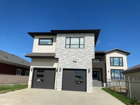 Two-storey stone and stucco building with two garage doors, an entrance and a concrete driveway