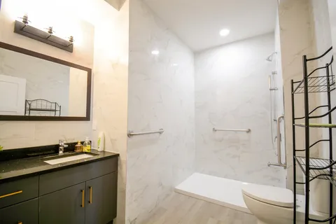 Bathroom with a walk-in shower, grab bars, a toilet and a dark vanity