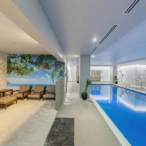 Indoor swimming pool beside chairs and a wall mural.