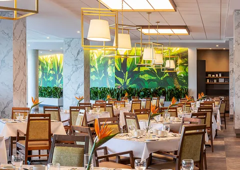 Dining room with set tables, pendant lighting and a leafy mural.