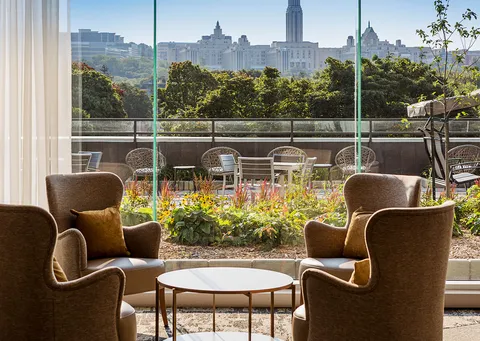 Lounge chairs beside windows overlooking a planted terrace.