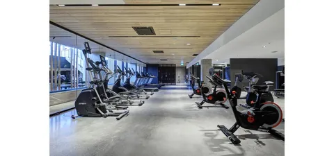 Fitness room with exercise bicycles and machines beside tall windows