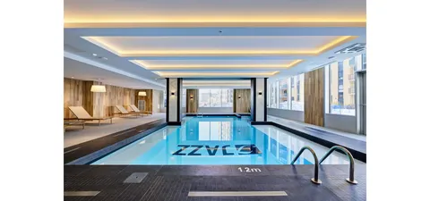 Indoor pool beneath a lit ceiling beside a row of tall windows