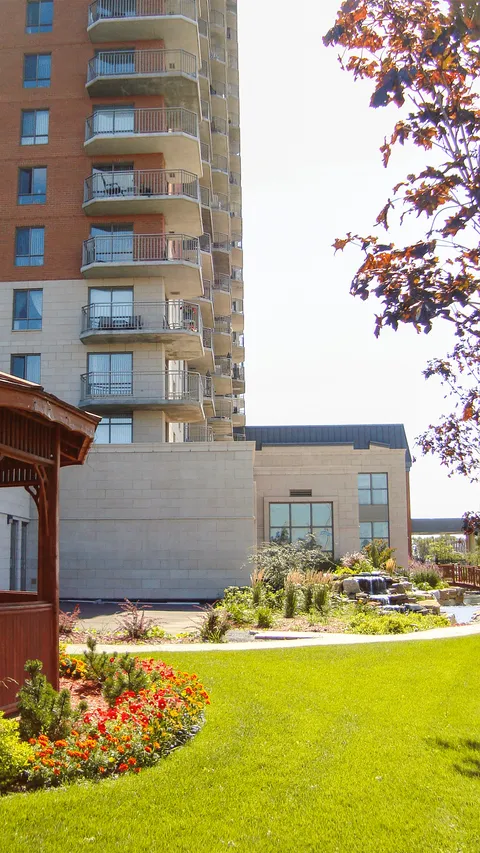 Lawn and flower beds beside a residence with balconies, a wooden gazebo and a small waterfall