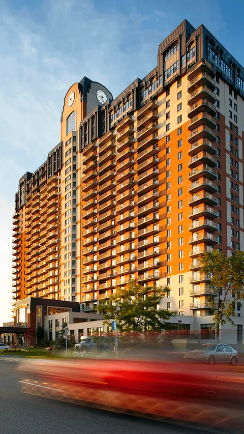 Tall residence with balconies, a clock tower and cars passing along the road