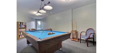 Billiards table beneath pendant lights beside a bookcase.