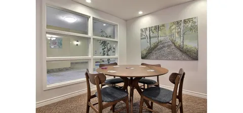 Common room with a round table, chairs and large windows.