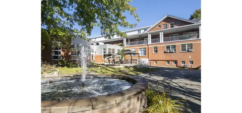 Circular fountain beside trees, paths and the residence.