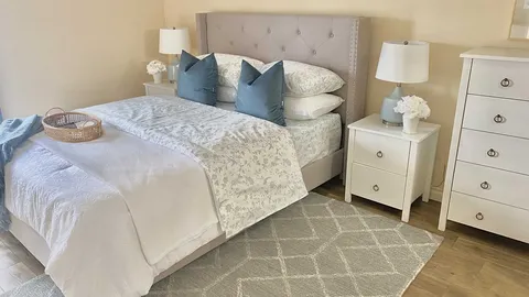 Bedroom with a tufted headboard, bedside lamps and white drawers.