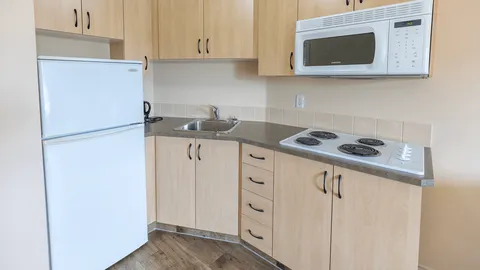 Kitchenette with light wood cabinets, refrigerator, microwave and stovetop.