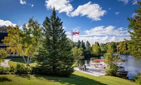 Lakeside lawn with trees, a Canadian flag and a docked pontoon boat