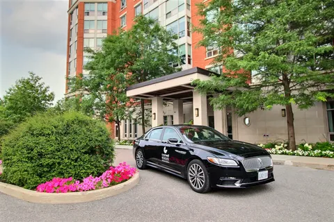 Covered residence entrance beside a black car and landscaped flower beds