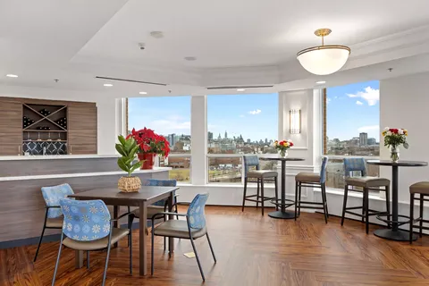 Room with small tables, chairs and large windows overlooking the city