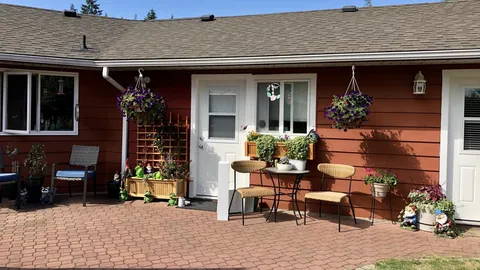 Residence doors opening onto a paved patio with tables and flower pots.
