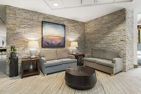 Room with two grey sofas, side tables, lamps and a landscape painting on stone walls