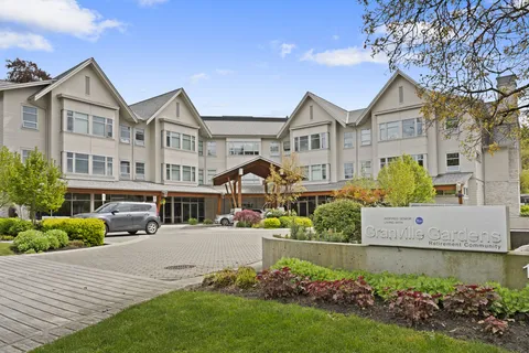Three-storey residence with gabled roofs, a covered entrance, driveway and planted garden beds