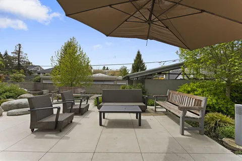 Patio with chairs, a bench, a coffee table, a large umbrella and planted garden beds