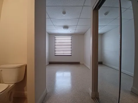 Empty room with a striped window blind, mirrored closet and toilet in the foreground