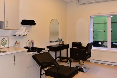 Salon with black chairs, mirrors and a washing basin.