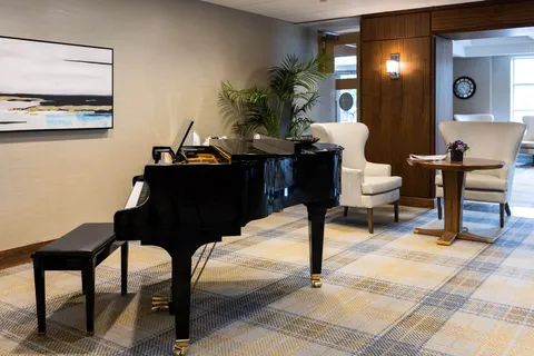 Black grand piano, upholstered armchairs, a round table and framed landscape art