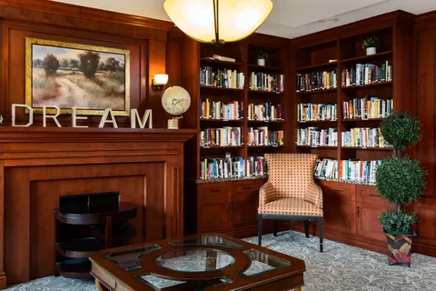 Library shelves, an armchair, a wooden mantel and framed landscape painting