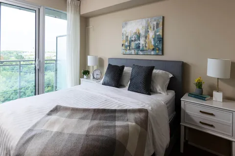 Bed with a dark padded headboard, bedside lamps and balcony doors