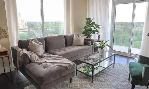 Sofa and glass coffee table beside balcony doors overlooking trees