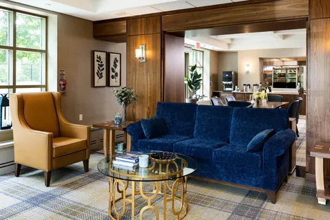 Blue sofa and yellow armchair beside a glass coffee table and framed botanical prints