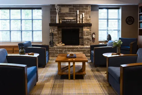 Blue armchairs and wooden tables around a stone fireplace with candles on its mantel